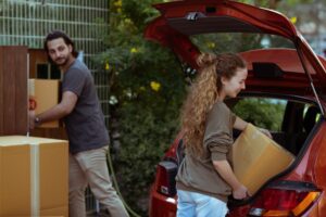 couple getting carton boxes out of red car while relocating in new home